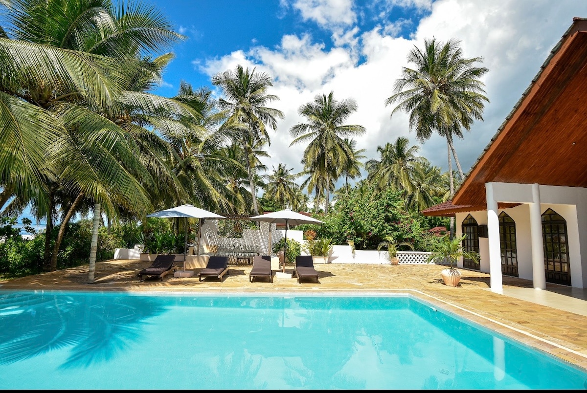 Pool with villa gable, palm grove and glimpse of ocean